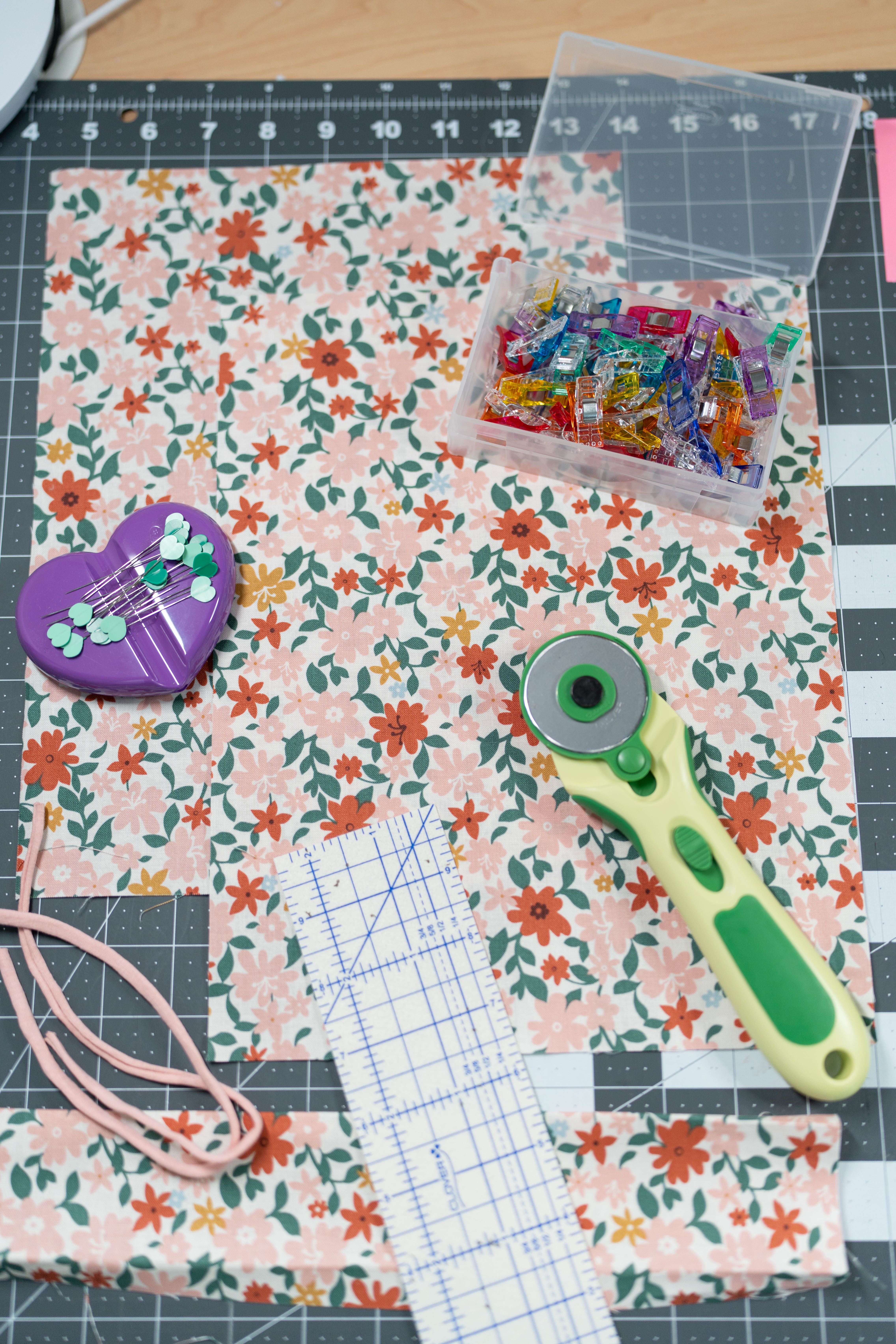 Happy Stitches sewing project supplies for a Crayon Wrap Roll, including fabric pieces, Clover Hot Ruler, Rotary Cutter, Heart-Shaped Pins, Wonder Clips, and Roll & Press