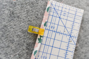 Happy Stitches sewing project supplies for a Crayon Wrap Roll, including fabric pieces, Clover Hot Ruler, Rotary Cutter, Heart-Shaped Pins, Wonder Clips, and Roll & Press