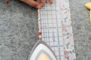 Happy Stitches sewing project supplies for a Crayon Wrap Roll, including fabric pieces, Clover Hot Ruler, Rotary Cutter, Heart-Shaped Pins, Wonder Clips, and Roll & Press